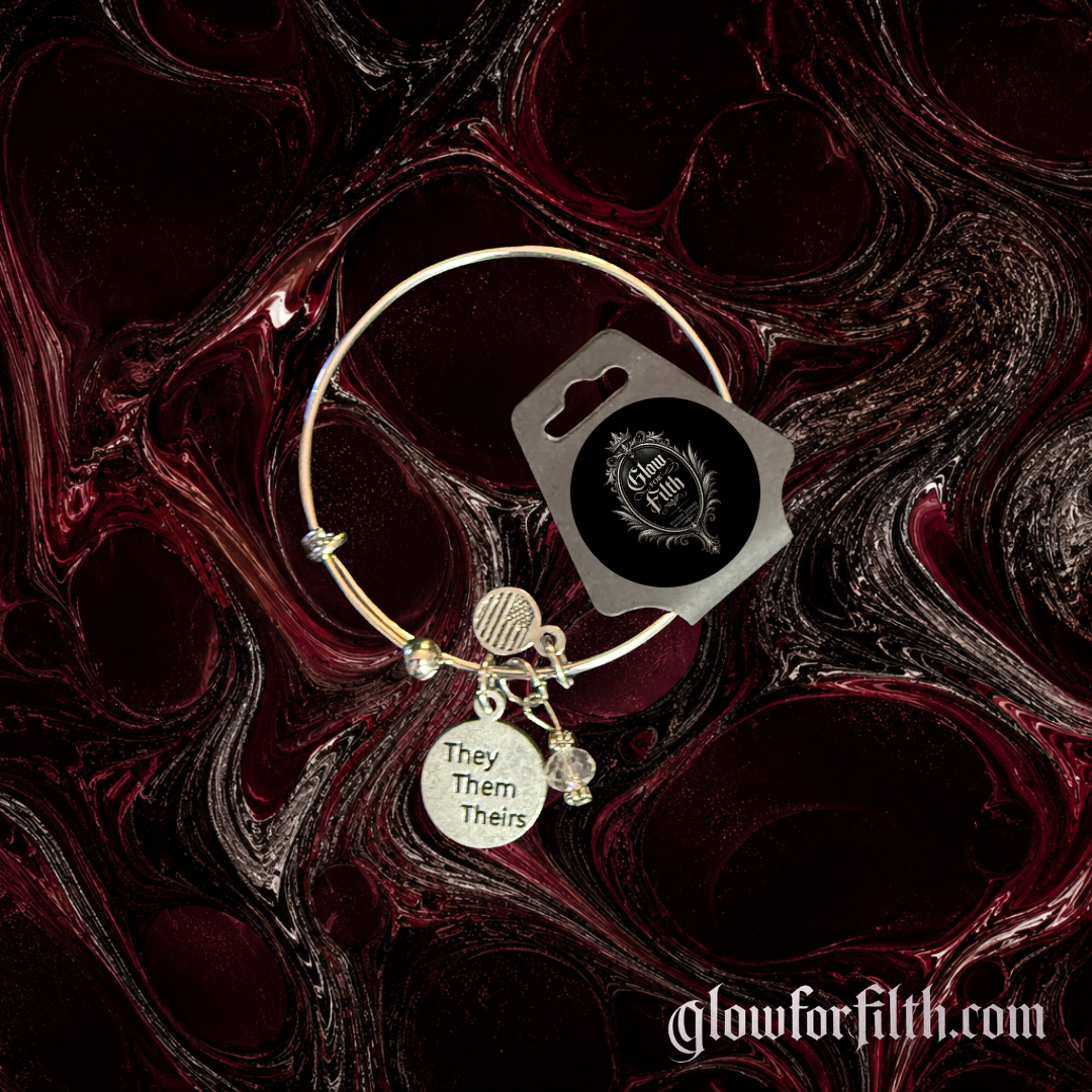 Silver-tone adjustable bracelet featuring a lead-free pewter They Them Theirs charm and crystal accent bead displayed on a gothic burgundy and black marbled background.