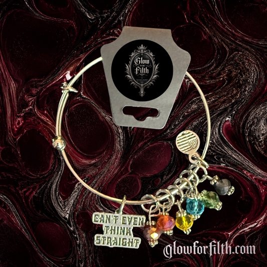 Silver-tone expandable bangle bracelet featuring a "Can't Even Think Straight" charm and multiple rainbow crystal accents displayed on a gothic burgundy and black marbled background.