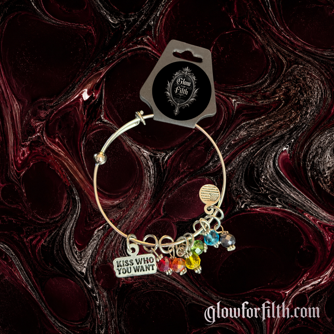 Silver-tone expandable bangle bracelet featuring a lead-free pewter Kiss Who You Want charm and rainbow crystal accents displayed on a burgundy and black gothic background.