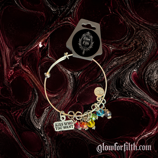 Silver-tone expandable bangle bracelet featuring a lead-free pewter Kiss Who You Want charm and rainbow crystal accents displayed on a burgundy and black gothic background.