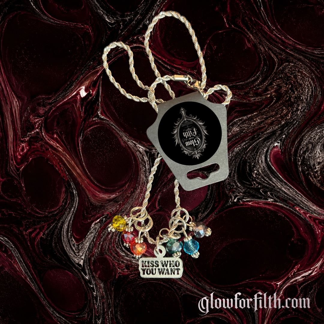 Silver-tone rope chain necklace featuring a lead-free pewter Kiss Who You Want charm accented with rainbow crystal beads on a burgundy and black gothic background.