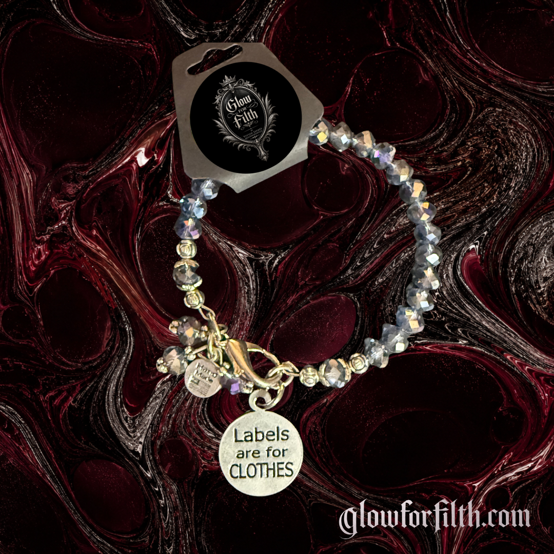 Faceted crystal bracelet featuring a lead-free pewter Labels Are for Clothes charm displayed on a burgundy and black gothic background.