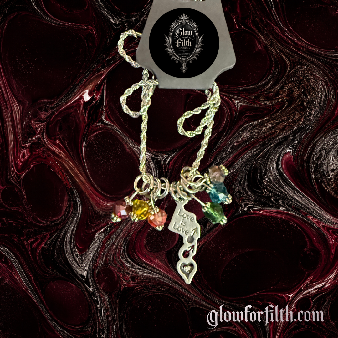 Silver-tone rope chain necklace featuring a lead-free pewter Love Is Love pendant with male-male symbols and rainbow crystal accents displayed on a gothic burgundy and black marbled background.