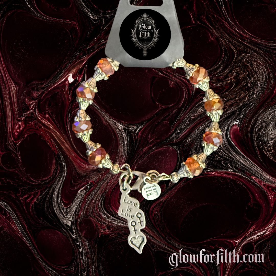 Handmade crystal bracelet featuring a lead-free pewter Love Is Love charm with female-female symbols and faceted crystal beads displayed on a gothic burgundy and black marbled background.