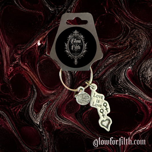 Silver-tone keychain featuring a lead-free pewter Love Is Love charm with female-female symbols displayed on a gothic burgundy and black marbled background.