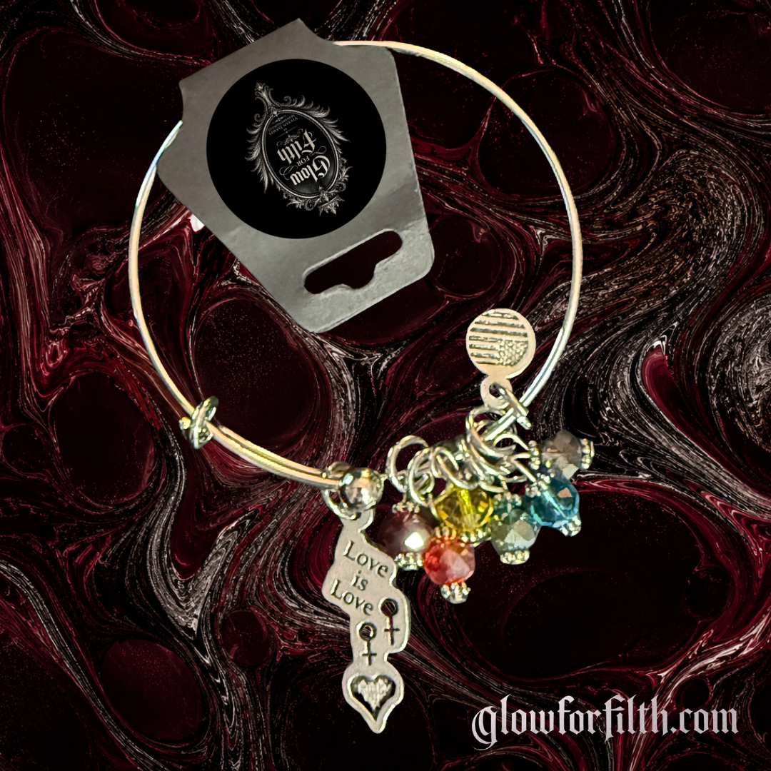 Silver-tone expandable bangle bracelet featuring a lead-free pewter Love Is Love charm with female-female symbols and rainbow crystal accents displayed on a gothic burgundy and black marbled background.