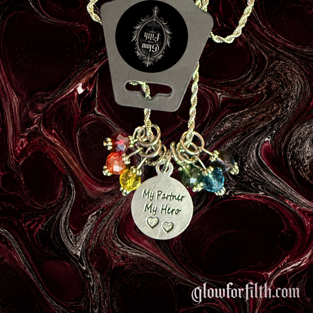 Silver-tone rope chain necklace featuring a lead-free pewter My Partner My Hero charm accented with rainbow crystal beads on a gothic burgundy and black marbled background detail shot.