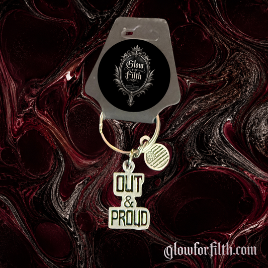 American pewter Out & Proud keychain with American flag accent charm displayed on Glow for Filth branded packaging.