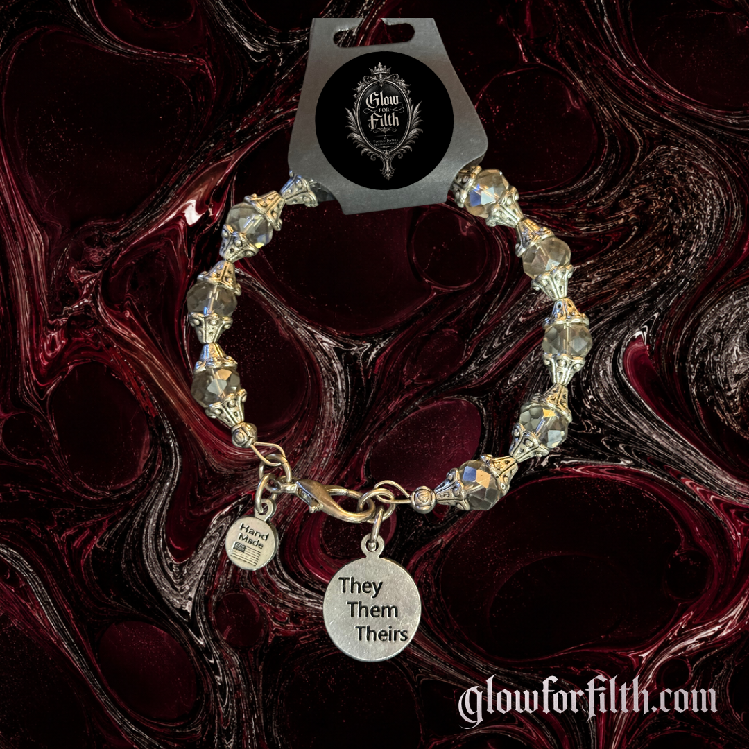 Handcrafted crystal bracelet featuring a lead-free pewter They Them Theirs pronoun charm with faceted iridescent crystal beads on a gothic burgundy and black marbled background.