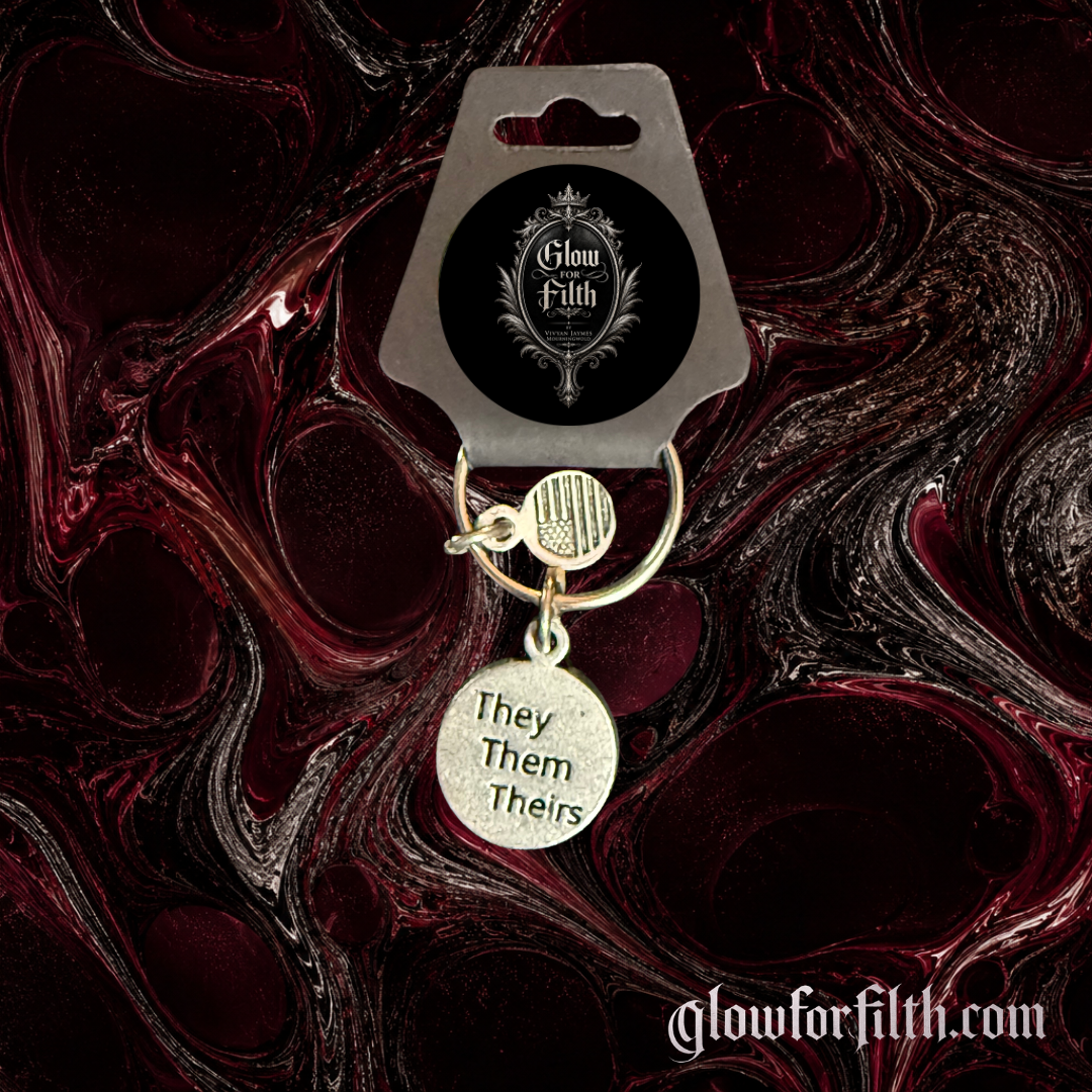 Silver-tone keychain featuring a lead-free pewter They Them Theirs pronoun charm displayed against a burgundy and black gothic marbled background.