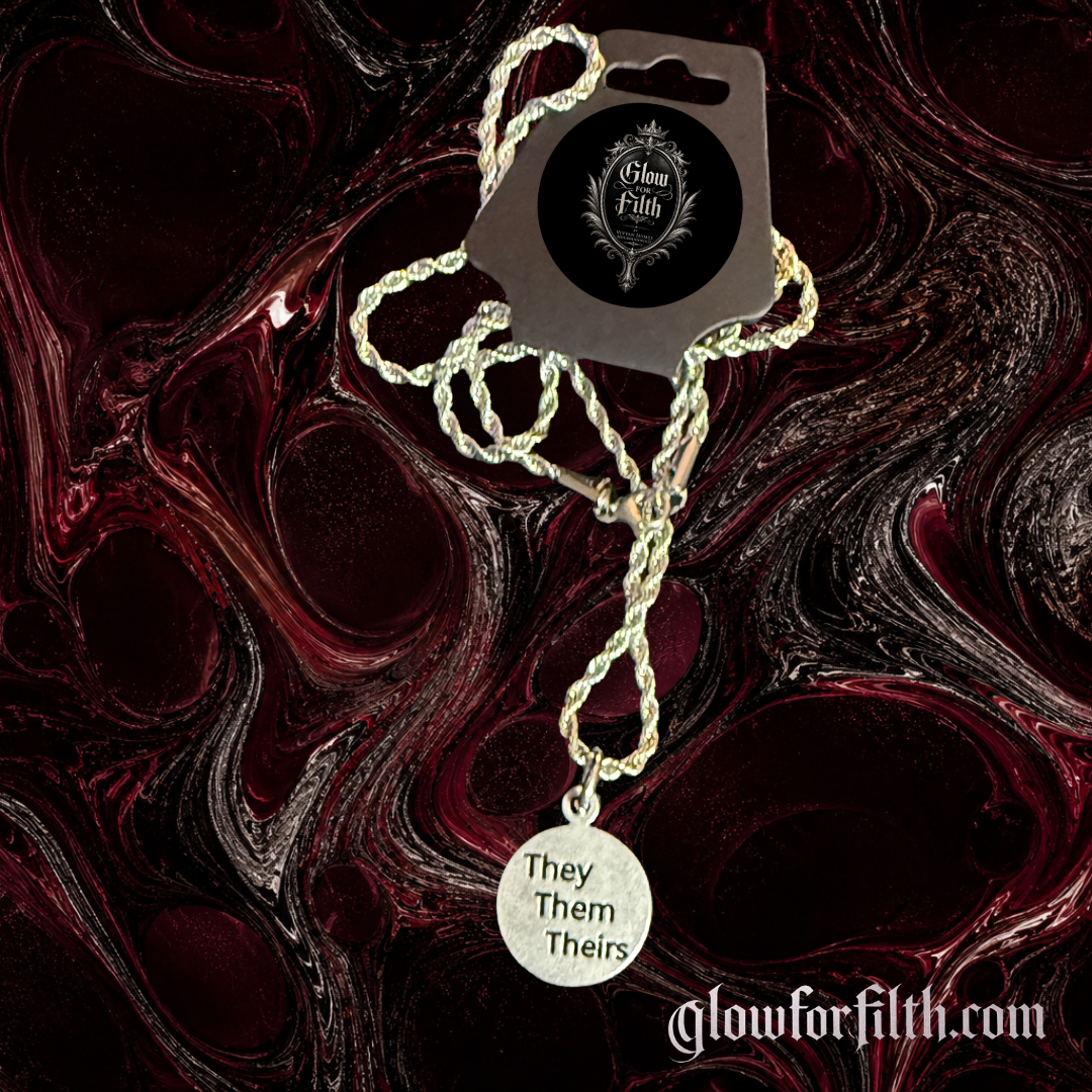 Silver-tone rope chain necklace featuring a lead-free pewter They Them Theirs pronoun charm displayed on a gothic burgundy and black marbled background.